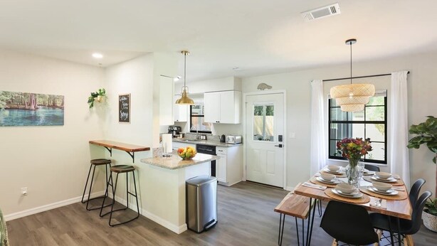 Una cocina moderna con una isla central, taburetes de bar, una mesa de comedor para seis personas e iluminación colgante.
