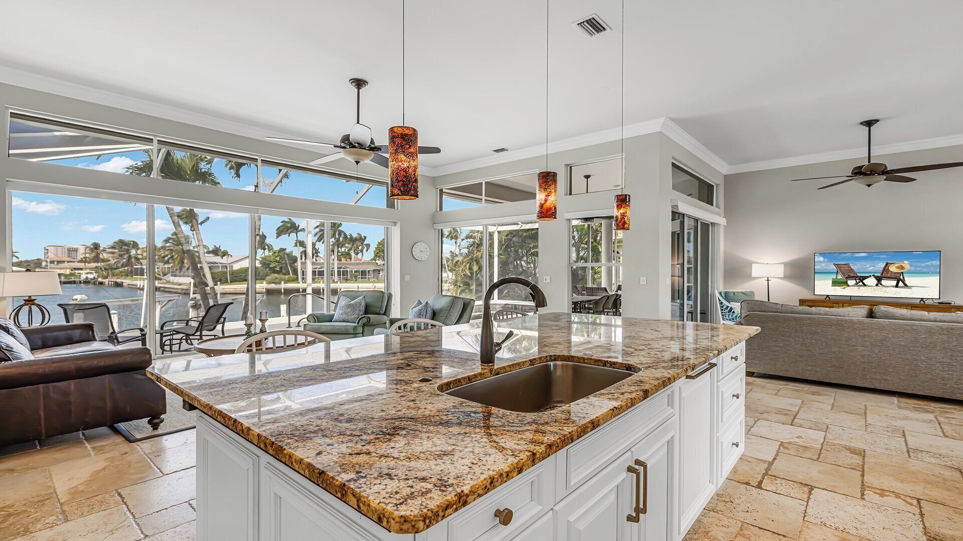 A spacious kitchen with a granite countertop, a large island with a sink, pendant lights, and a view of the outdoors.