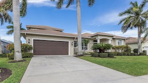 A residential house with a garage, palm trees, and a well-maintained lawn. - Spacious 4 bedroom/3 bath pool home w/Western exposure (Marco Island)