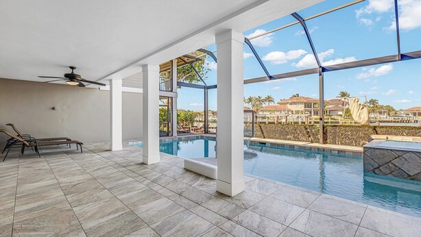 Una piscina con vistas a una zona residencial, un ventilador de techo y sillas de descanso.
