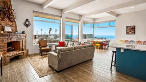 Amplia sala de estar con chimenea, un sofá y un comedor con vista al océano.