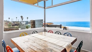 Un comedor con mesa de madera y sillas coloridas, con vistas a una playa y al océano.