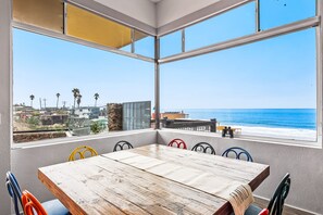 Une pièce dotée d’une grande fenêtre donnant sur une plage, d’une table en bois et de chaises colorées.