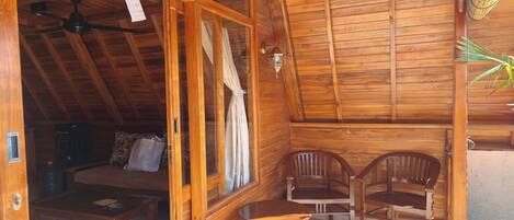 Una cabaña de madera con una cama, dos sillas, una mesa, un ventilador de techo y una ventana con cortinas.