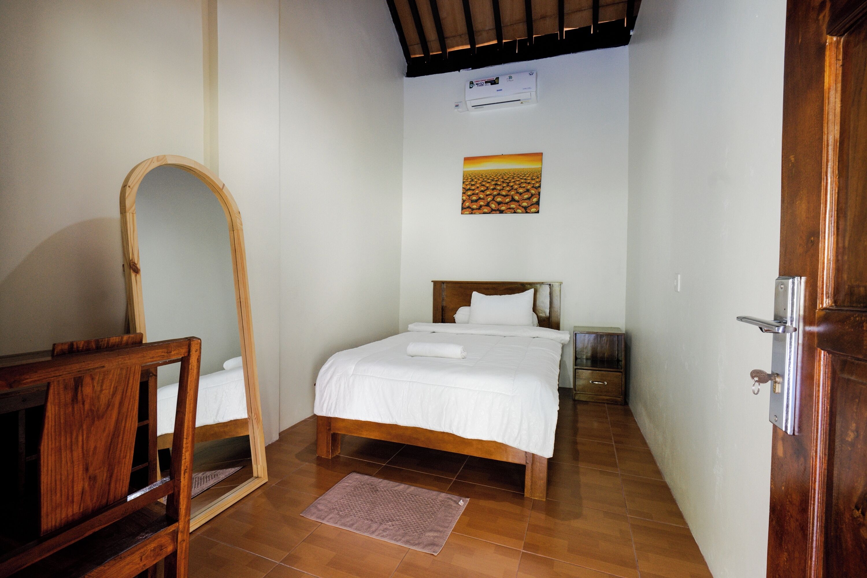A bedroom with a bed, a wooden dresser, a mirror, a wall-mounted air conditioner, and a painting.