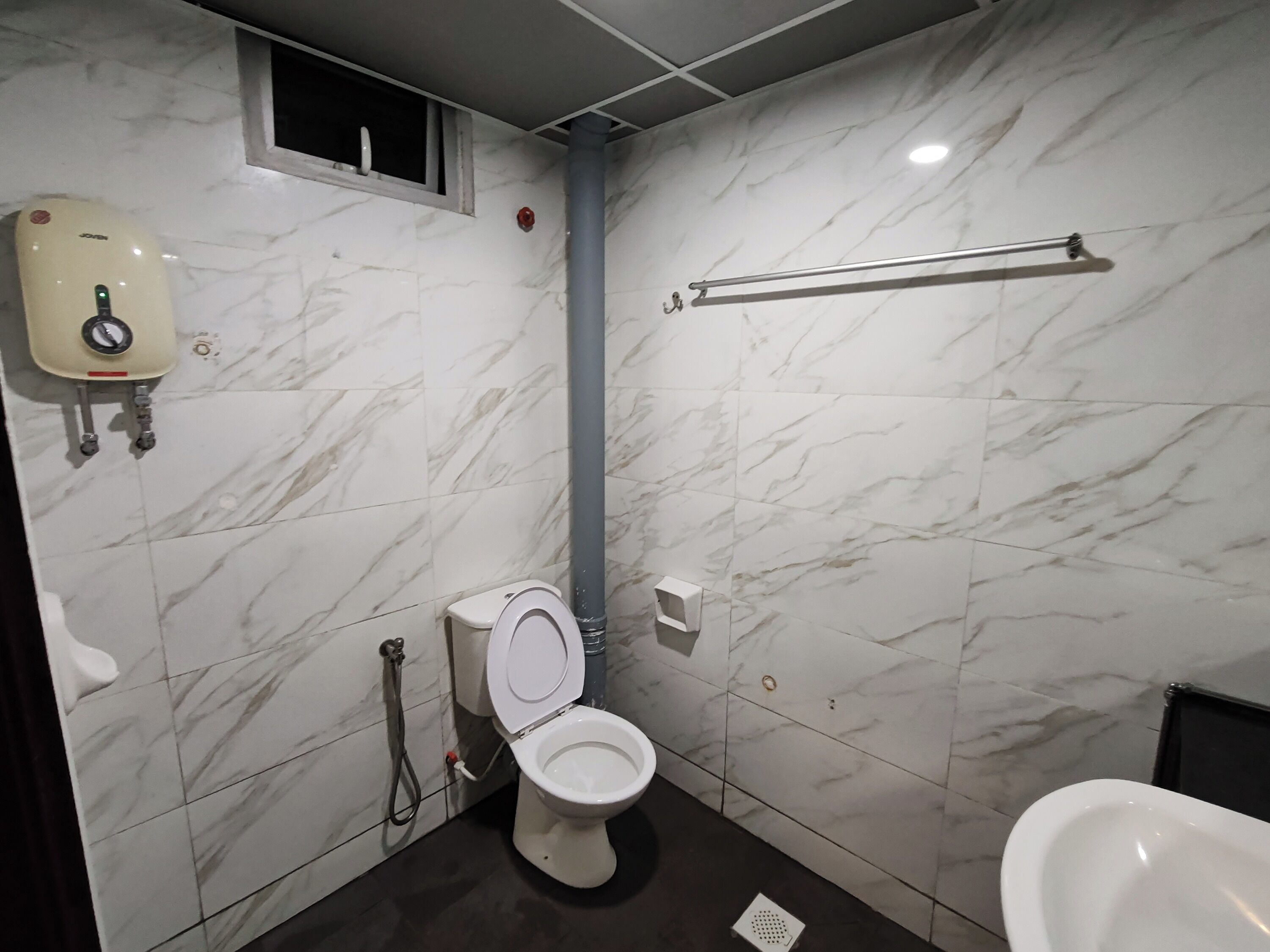 Un baño con inodoro, bidé, secador de manos y un perchero para toallas.