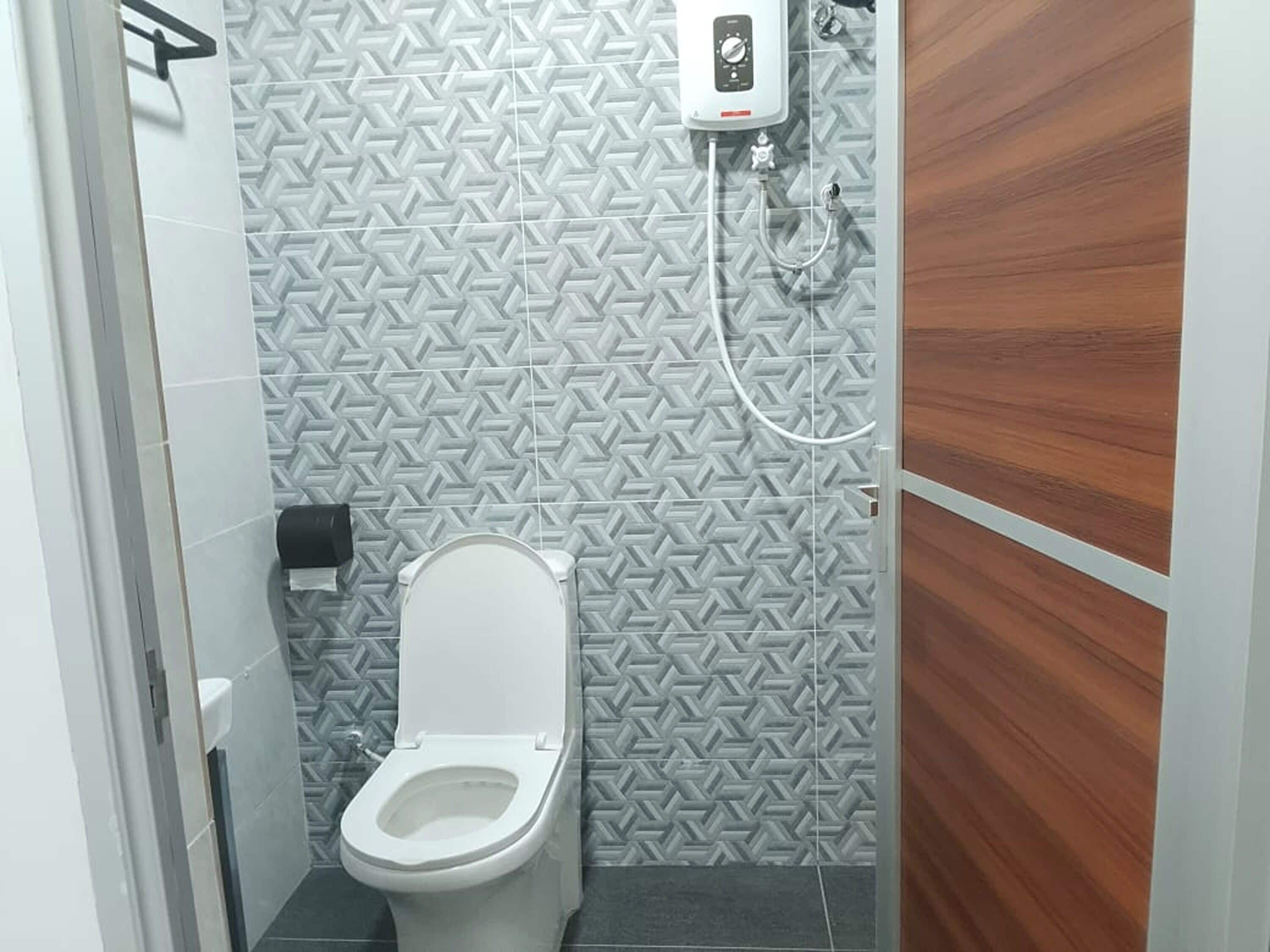 A small bathroom with a toilet, a hand dryer, and a showerhead.