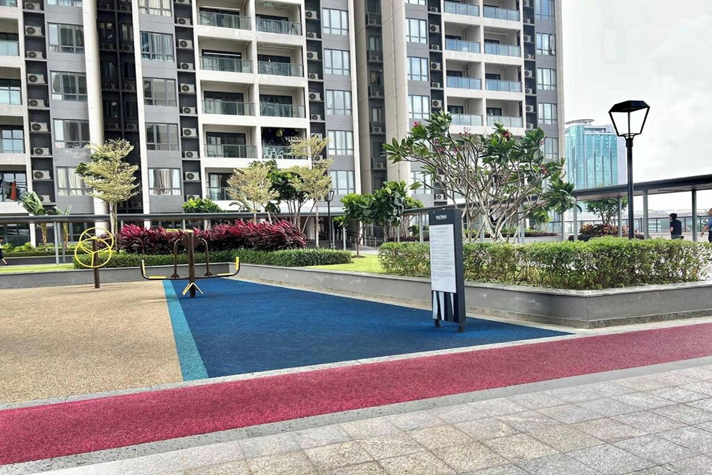 A residential building with multiple balconies, a playground with exercise equipment, and a landscaped area with trees and shrubs.