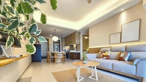 A modern living room with a sofa, a dining area, and a kitchen in the background. - R&F Princess Cove Designer Suites By Neo (Johor Bahru)