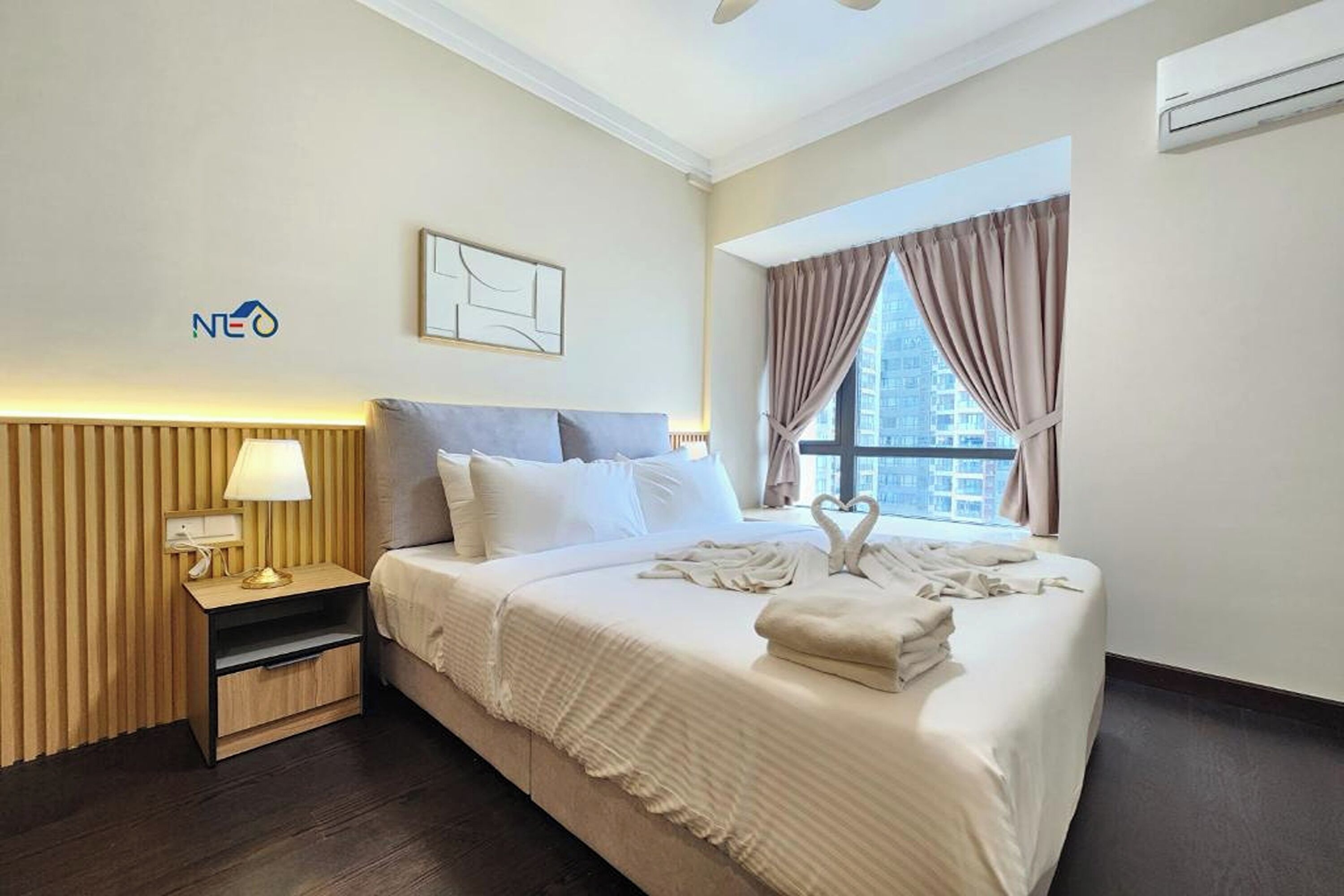 A hotel room with a bed, a nightstand, a lamp, a wall-mounted air conditioner, and a window with curtains.