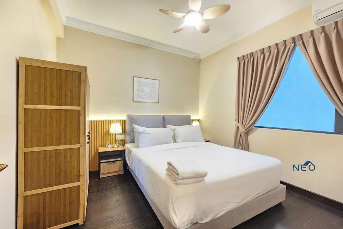 A hotel room with a bed, a nightstand, a wooden wardrobe, a ceiling fan, and a window with curtains.