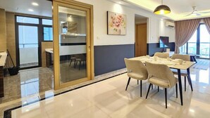 A modern dining area with a glass partition, a dining table with chairs, a ceiling fan, and a television. - R&F Princess Cove Designer Suites By Neo (Johor Bahru)