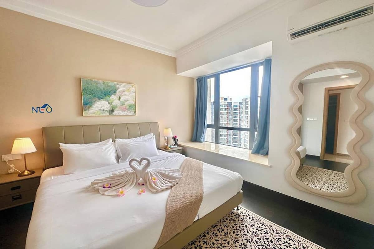 A hotel room with a bed, a painting, a window with a view, and a mirror.