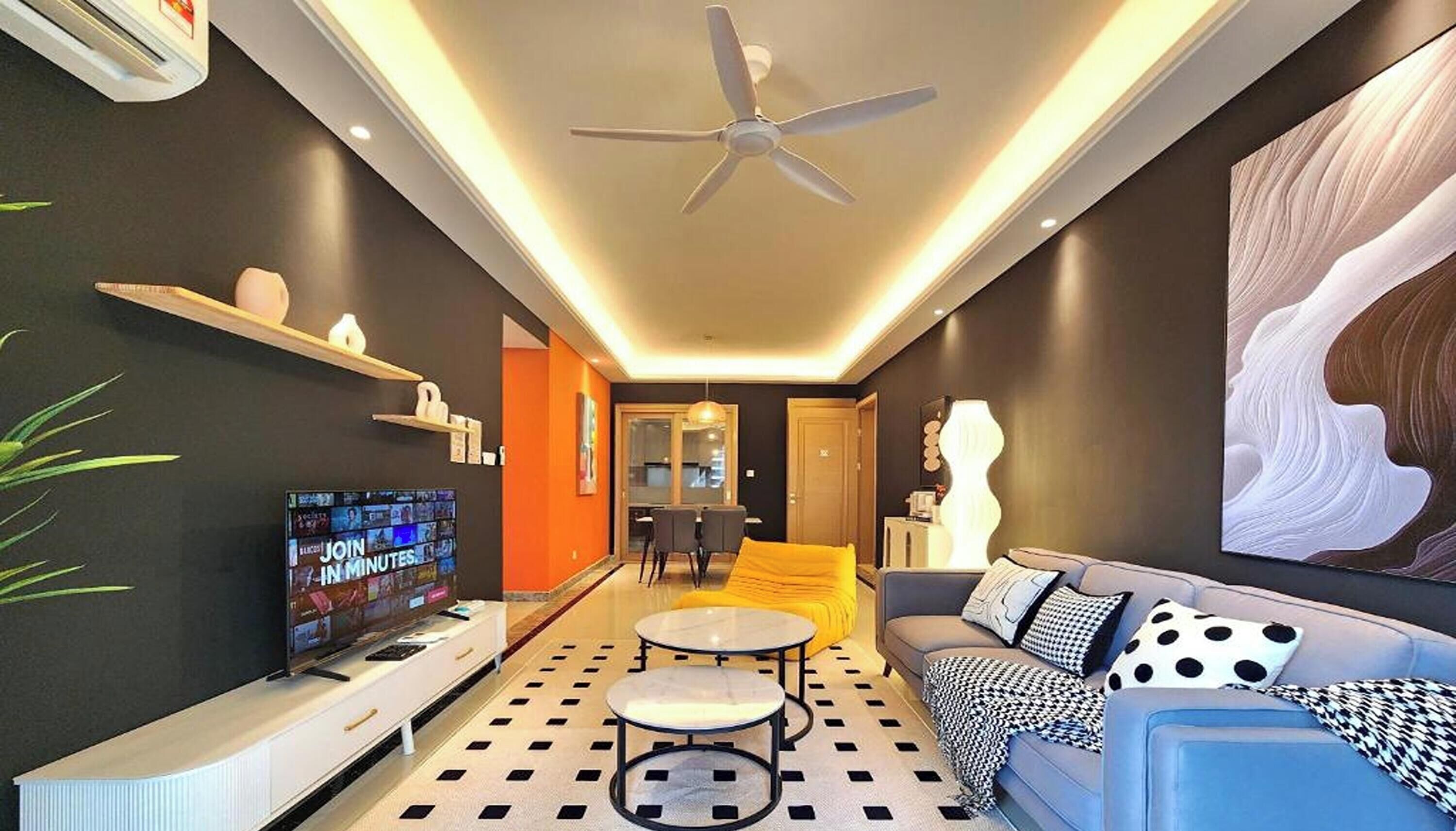 A modern living room with a flat-screen TV, a ceiling fan, a sofa, a coffee table, and a dining area with chairs.
