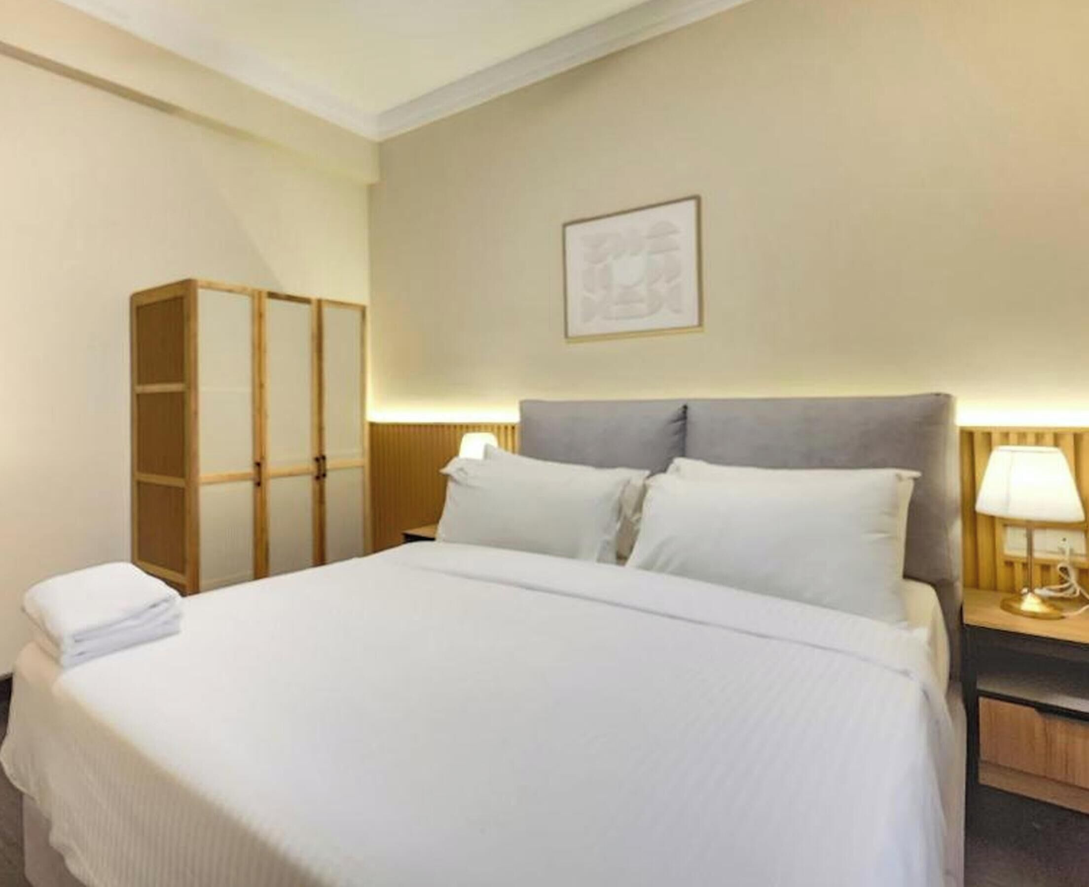 A hotel room with a bed, a wardrobe, a nightstand, and a wall-mounted lamp.