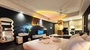 A modern hotel room with a bed, a desk, a television, a mirror, and a kitchenette. - R&F Princess Cove Designer Suites By Neo (Johor Bahru)
