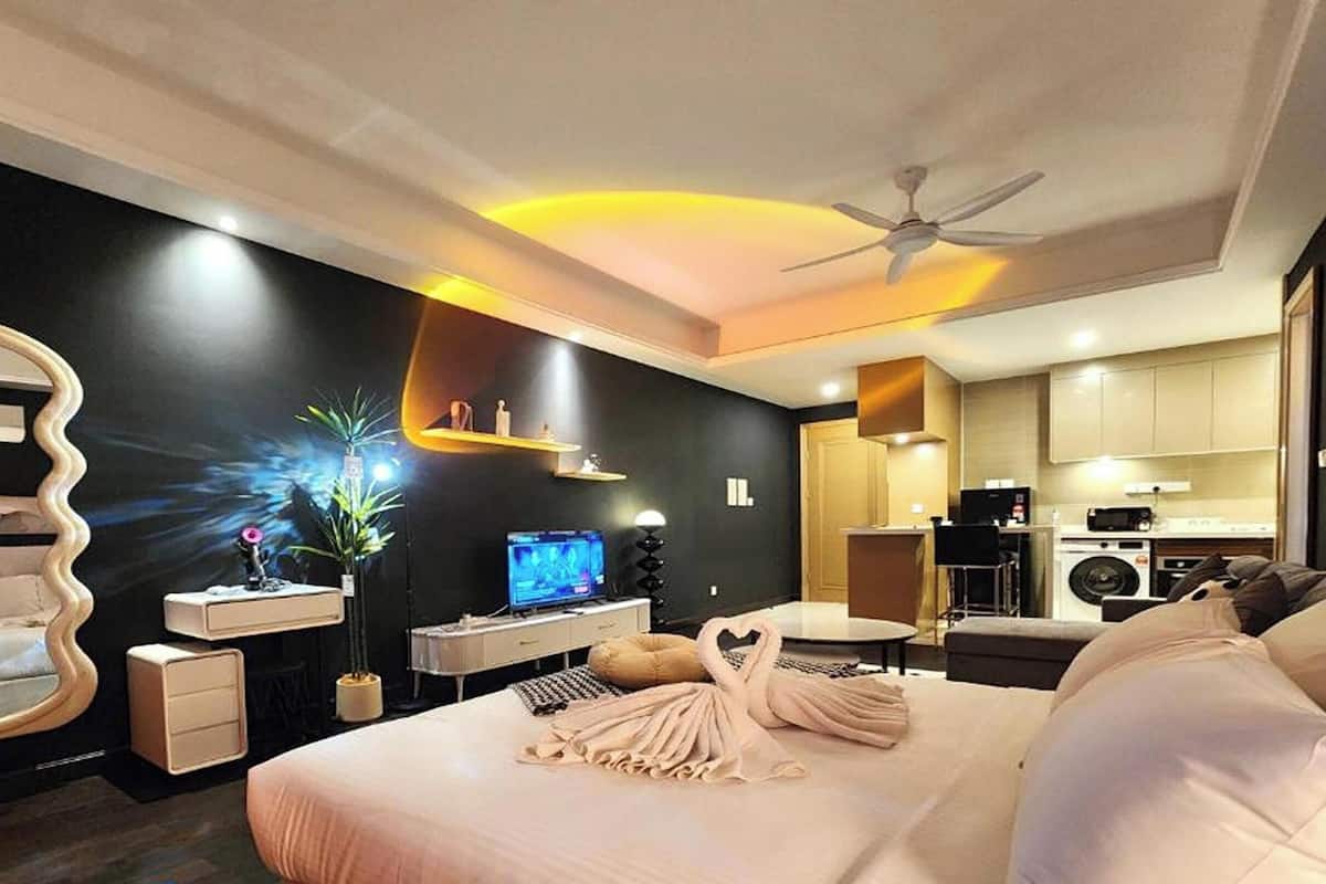 A modern hotel room with a bed, a desk, a television, a mirror, and a kitchenette.