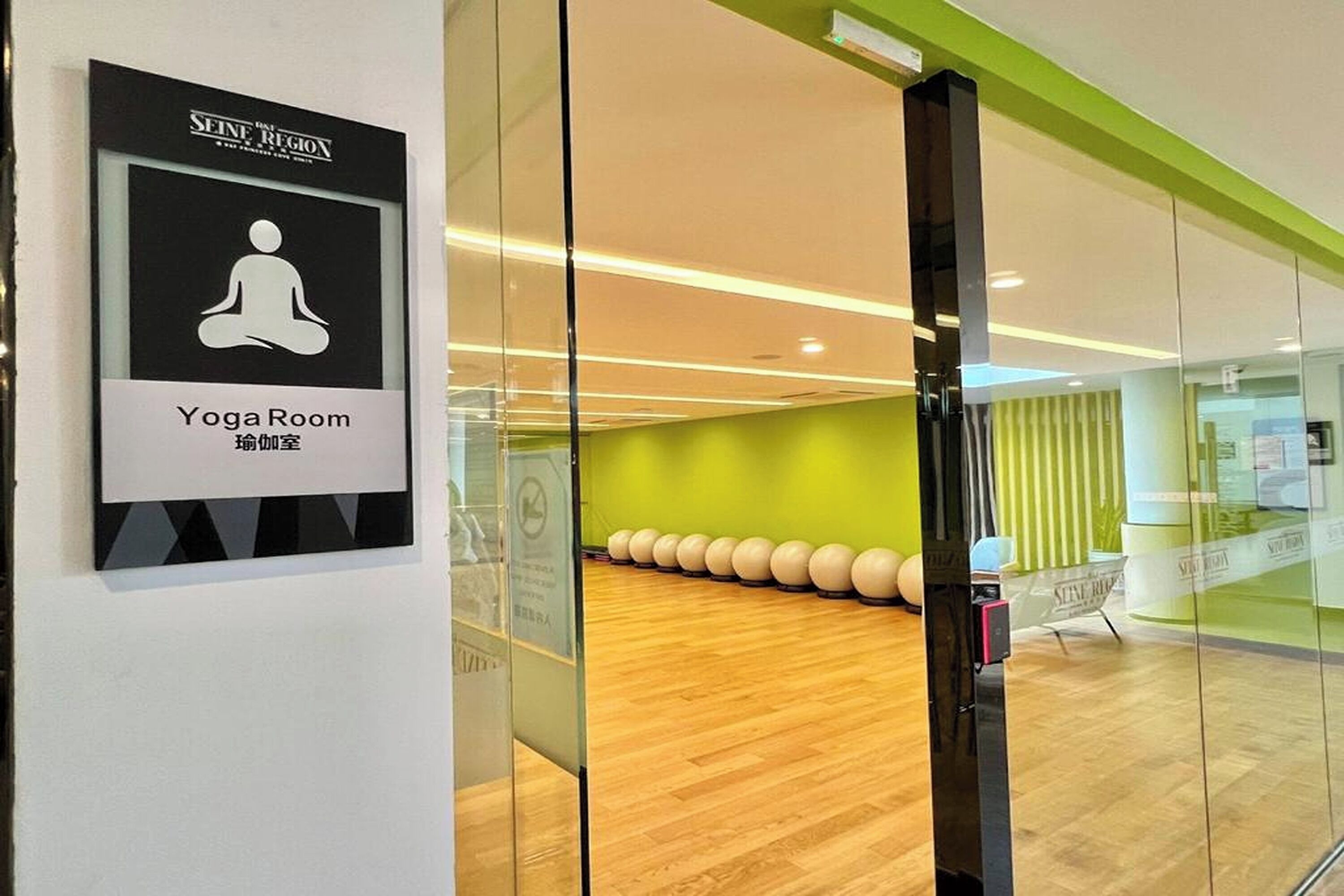 Una sala de yoga con un cartel que indica su función, suelo de madera y pelotas de ejercicios al fondo.