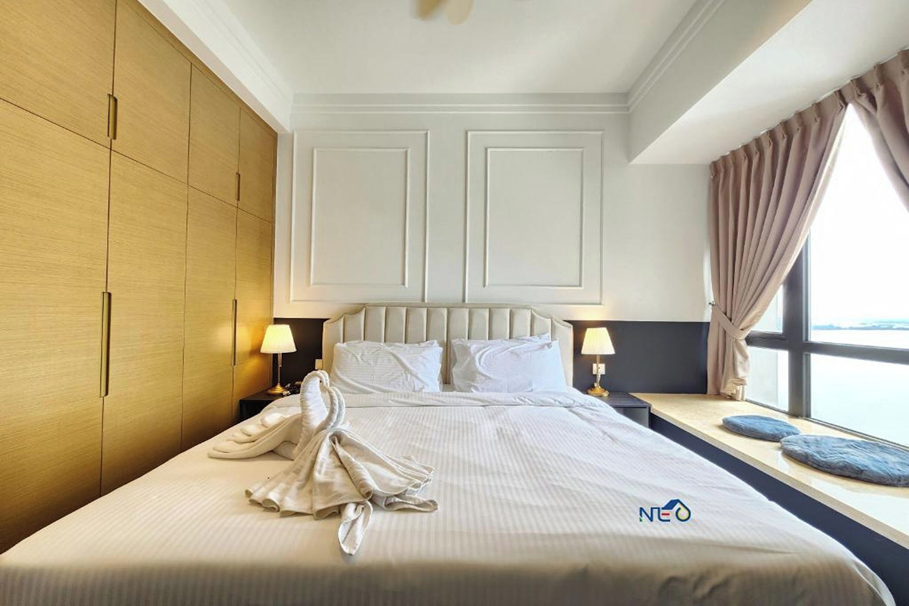 Habitación de hotel con una cama grande, dos mesitas de noche con lámparas, una ventana con cortinas y vistas al mar.