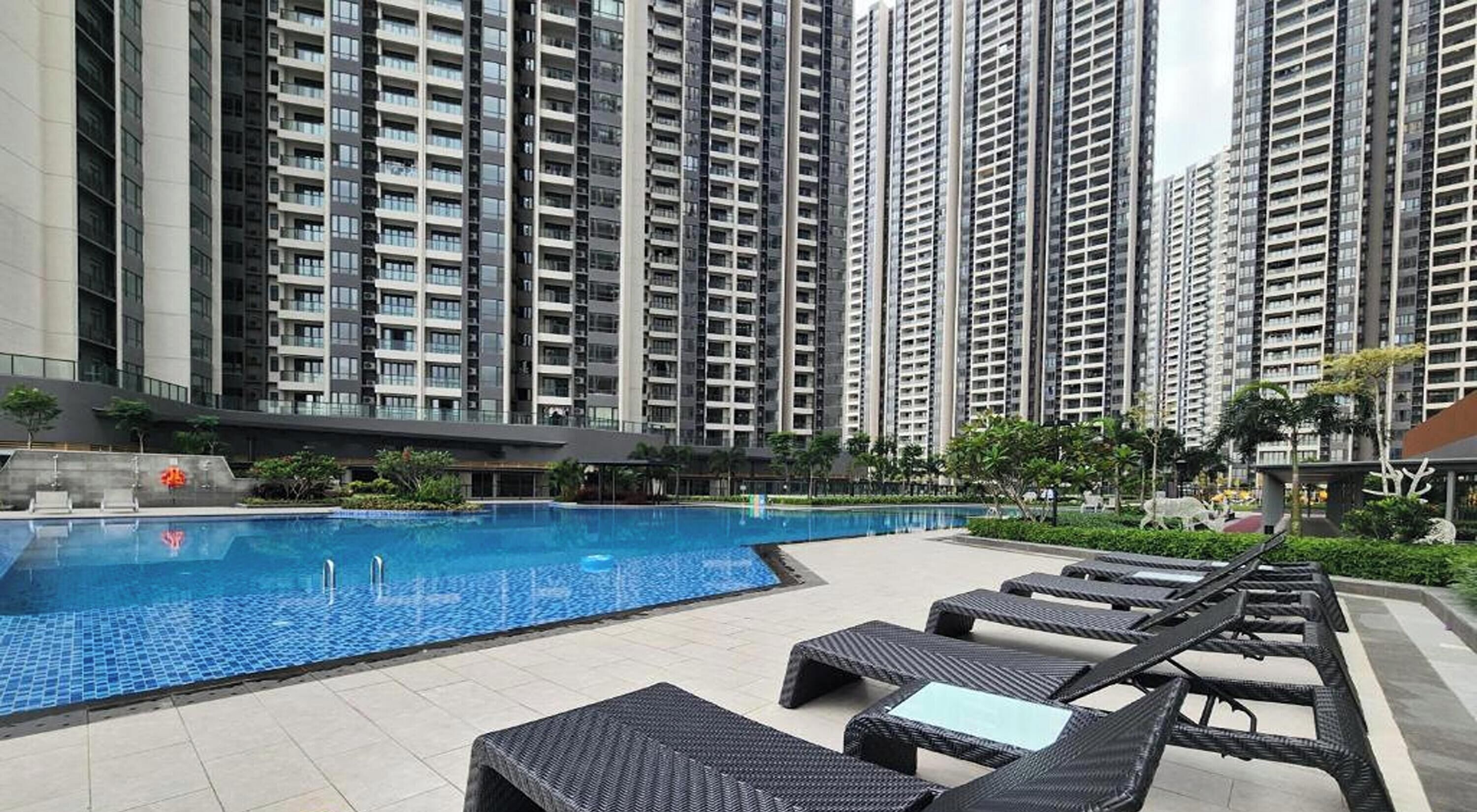 A swimming pool with lounge chairs, surrounded by high-rise residential buildings.