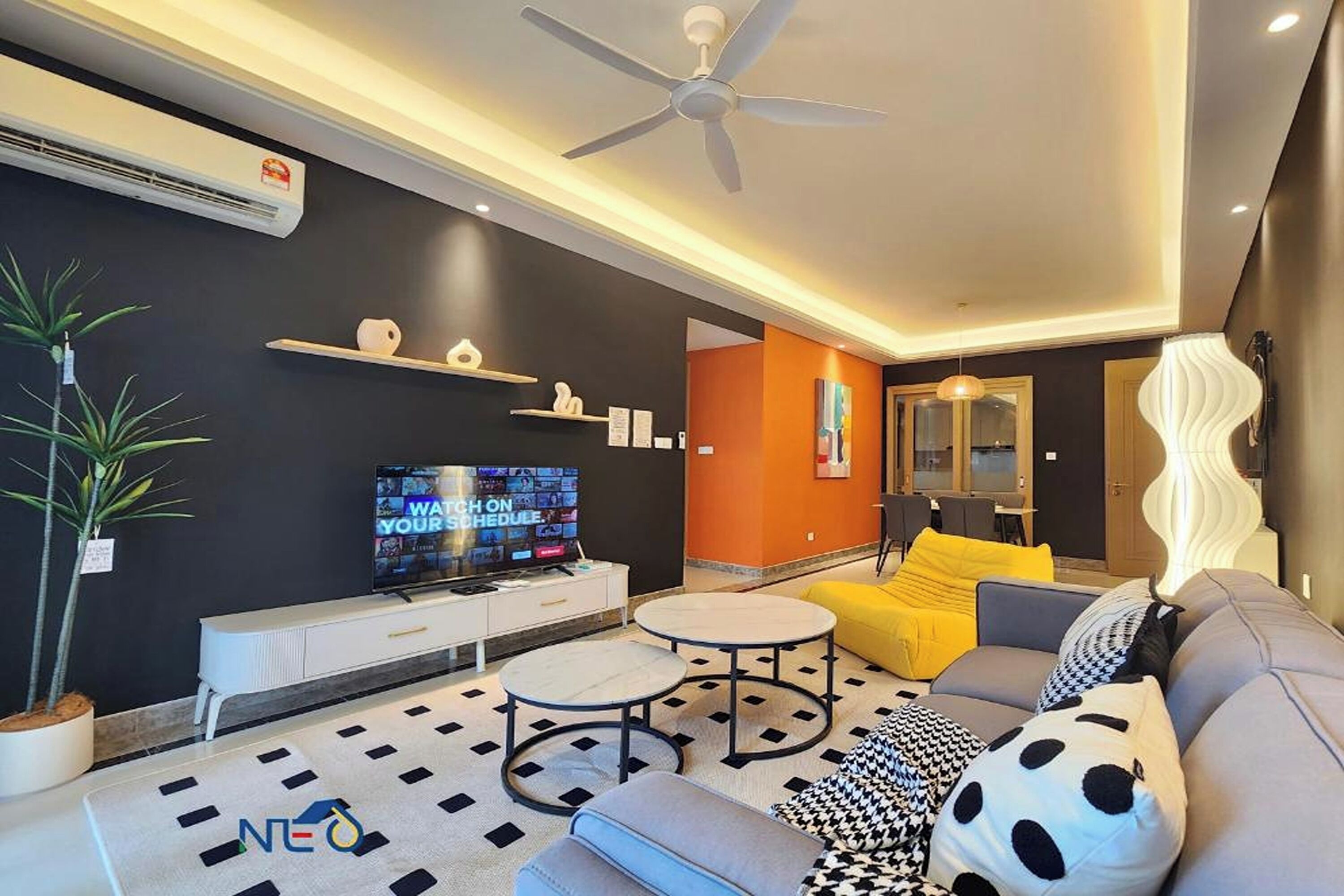 A modern living room with a flat-screen TV, ceiling fan, sofa, and decorative pillows.