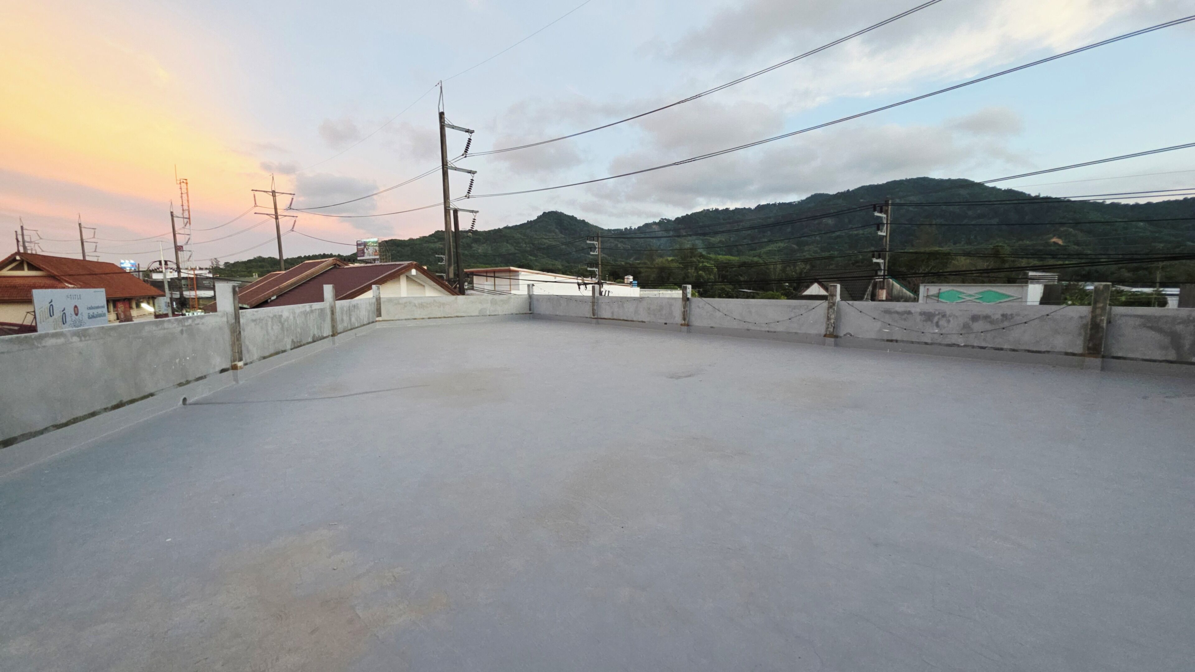 A rooftop terrace with a concrete floor, surrounded by buildings and power lines, overlooking a hilly landscape.