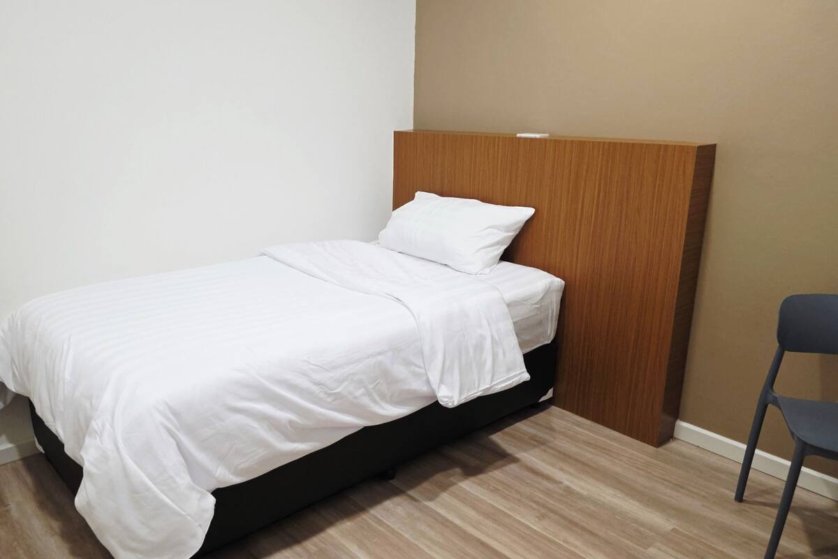 Uma cama de solteiro com cabeceira de madeira em quarto com piso de madeira e parede lisa.