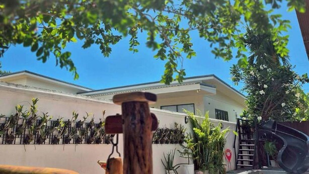 A swimming pool with a view of a modern building, surrounded by plants and a wooden deck. - Baan Pink Pool Villa Pattaya (Bang Lamung)