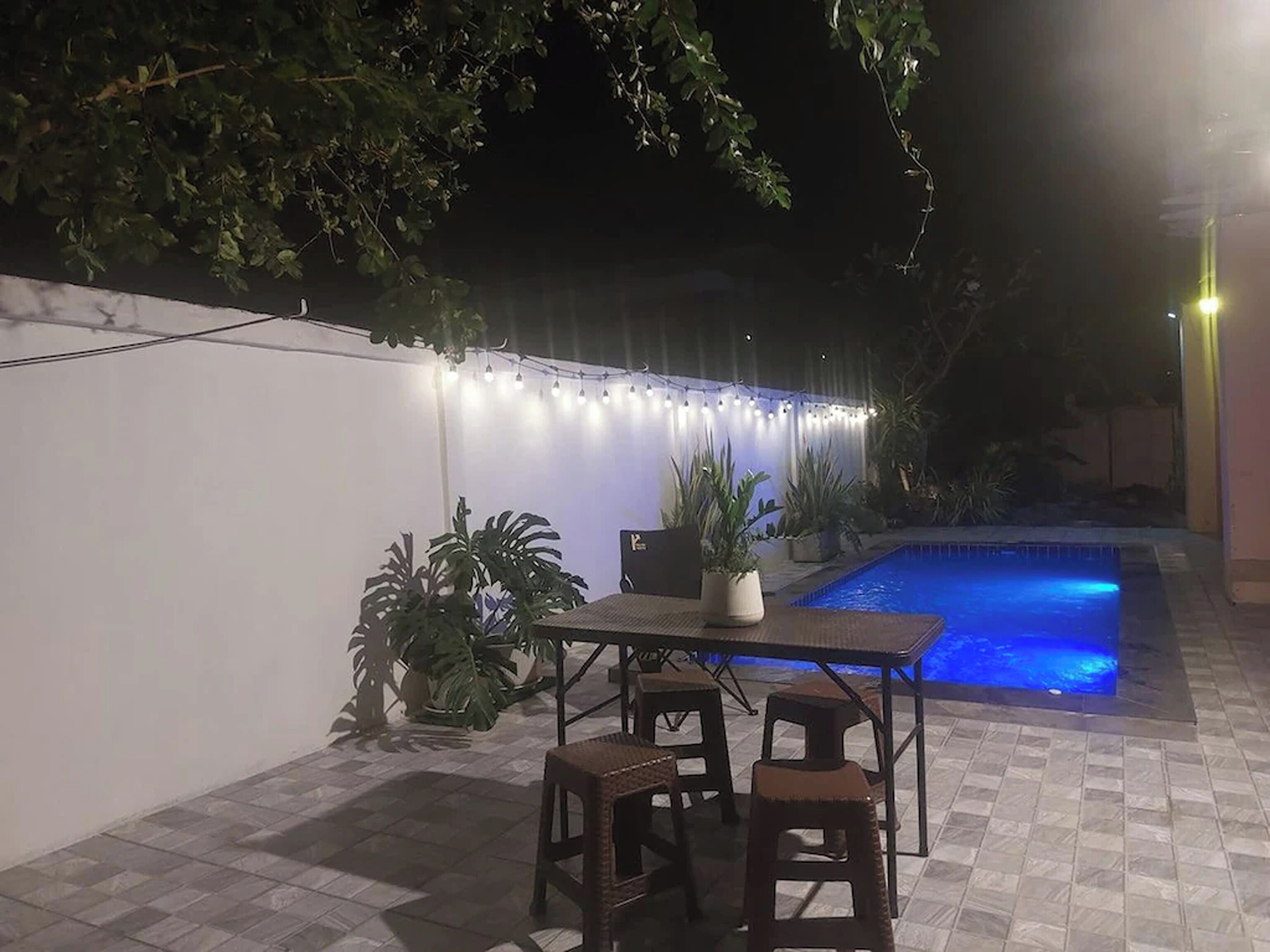 Een terras buiten met een zwembad, lichtjes en potplanten.