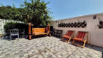 Eine Terrasse mit einer Holzbank, zwei gestreiften Liegestühlen und einem gefliesten Boden.