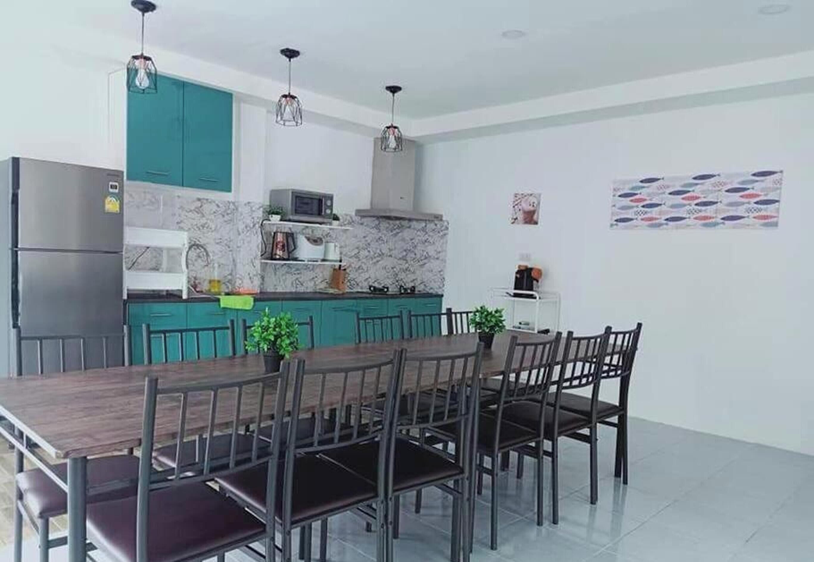 A modern kitchen with teal cabinets, a marble backsplash, a dining table with chairs, and pendant lighting.