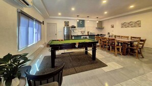 A modern living space with a pool table, dining area, kitchen, and a large window. - Baan Pink Pool Villa Pattaya (Bang Lamung)