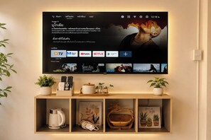 A flat-screen TV mounted on a wall with a selection of streaming services and a shelf below displaying various items. - Dad N Mom'S House By Thongnak Apartment (Pattaya)