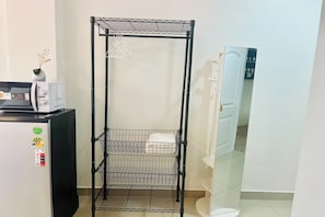 Une étagère métallique à plusieurs niveaux, un four à micro-ondes, un réfrigérateur et une porte avec un miroir.