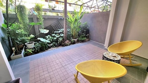 A covered patio with tiled flooring, yellow wicker chairs, a small round table, and various potted plants. - Dad N Mom'S House By Thongnak Apartment (Pattaya)