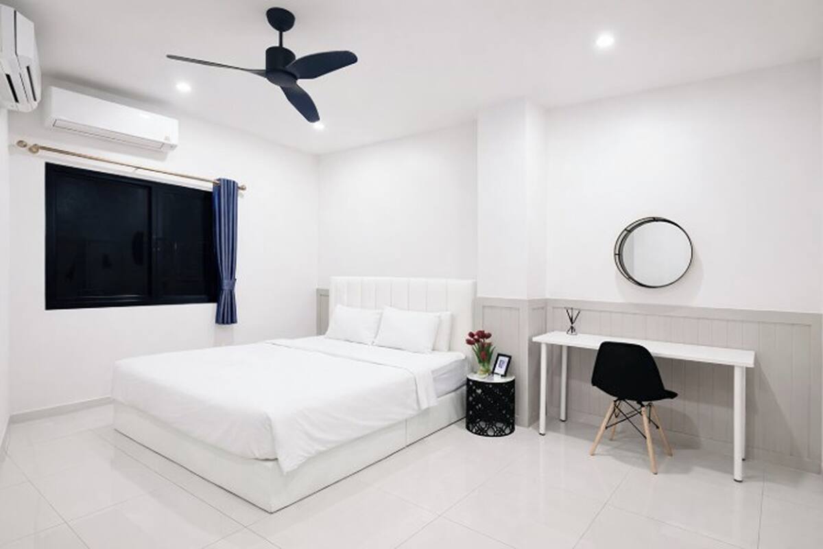 Un dormitorio con cama, escritorio, silla, ventilador de techo y ventana con cortinas.