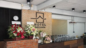 A hotel reception desk with a brick wall, a clock, and floral arrangements. - Teatel Ratchada (Bangkok)