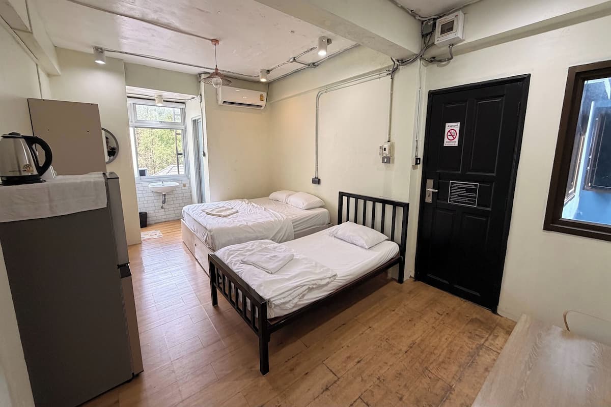 Una habitación con dos camas, un lavamanos, una tetera y una puerta con un cartel.