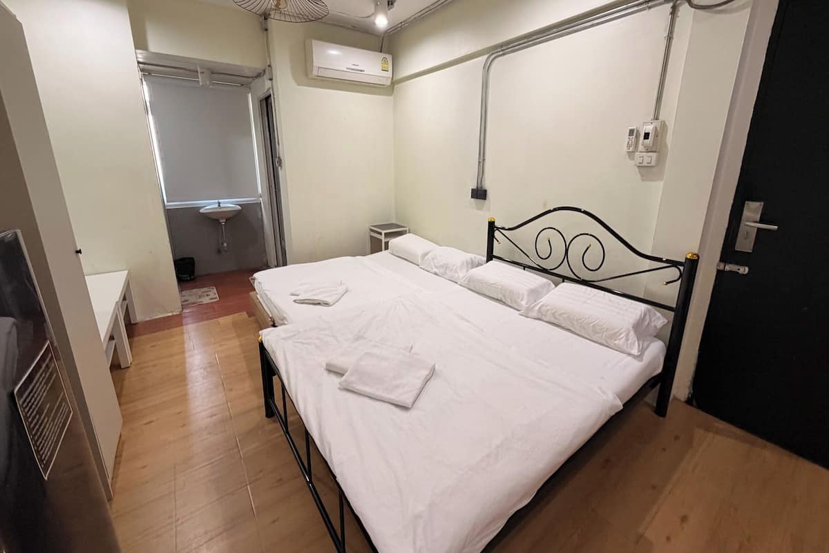 Un dormitorio con cama, mesita de noche, ventana, aire acondicionado instalado en la pared y puerta.