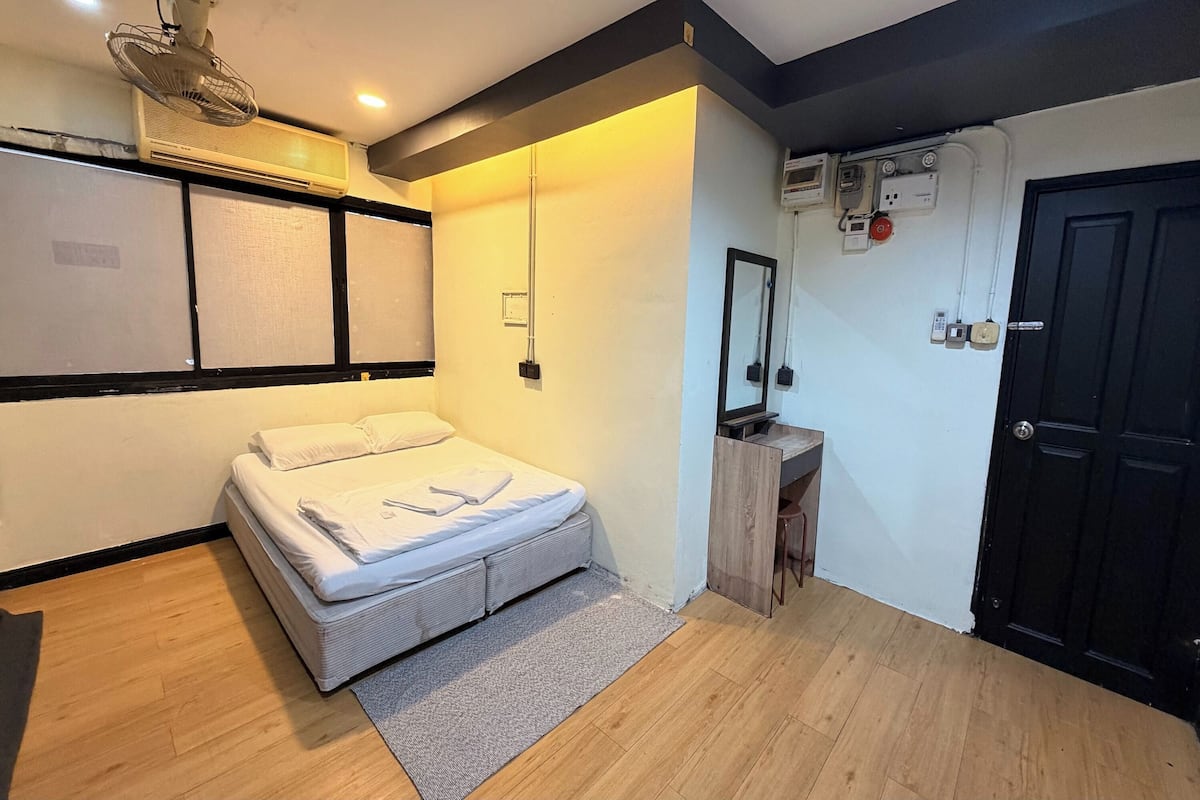 Un dormitorio con cama, escritorio, silla, unidad de aire acondicionado, puerta y ventana con persianas.