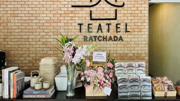A brick wall with a sign reading 'TEATEL RATCHADA' and a display of items including books, a vase with flowers, and packaged goods. - Teatel Ratchada (Bangkok)