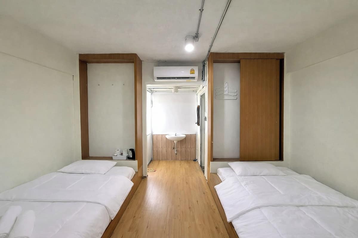 Habitación de hotel con dos camas, suelo de madera, un lavamanos y un equipo de aire acondicionado.