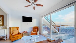 Ein modernes Wohnzimmer mit großem Fenster, zwei Ledersesseln, einem weißen Couchtisch und einem Deckenventilator.