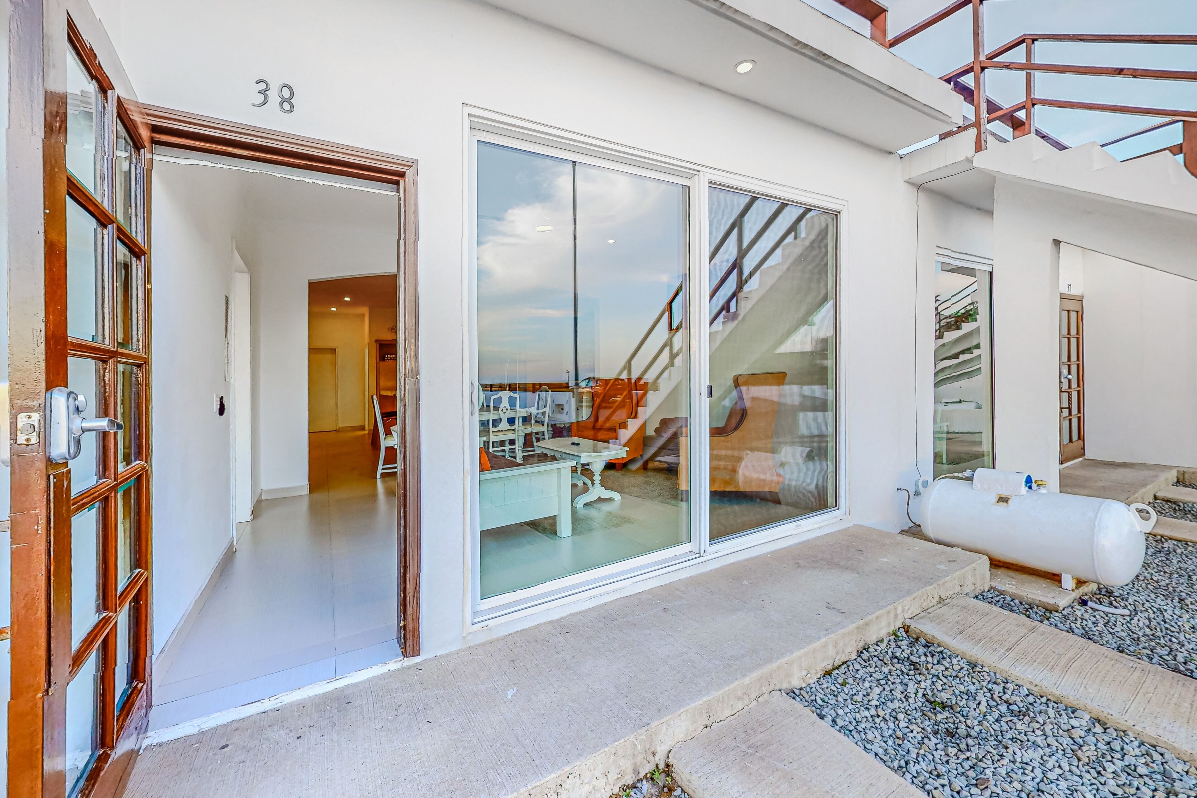 Un edificio moderno con un gran escaparate de vidrio, una escalera y una habitación visible con muebles.