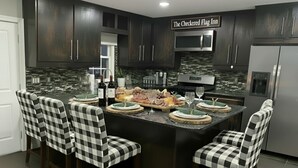 Una cocina con armarios de madera oscura, una isla central con mantel a cuadros, y un letrero que dice 'The Checkered Flag Inn'.
