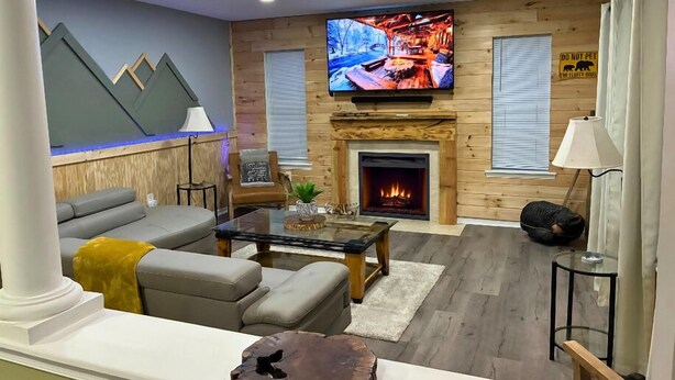 Una sala de estar con chimenea, televisor montado en la pared y un sofá.