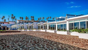 Ein modernes Hotel mit einem courtyard aus Steinplatten, Palmen und blauem Himmel.