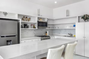 A modern kitchen with white cabinetry, a stainless steel refrigerator, a built-in microwave, and a gas stove. - Dog-friendly retreat with ocean-view rooftop deck, pool, hot tub, & kitchen (Rosarito)