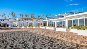 Un’area esterna pavimentata con edifici moderni, palme e un cielo azzurro intenso.
