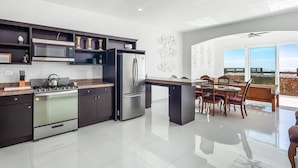 A modern kitchen with stainless steel appliances, a dining area with a wooden table and chairs, and a large window offering a view. - Bright dog-friendly home with heated pool, hot tub, streaming, & ocean views (Rosarito)